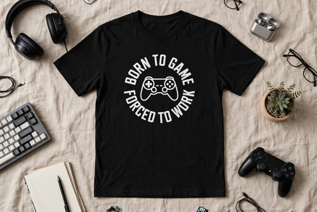 Flat lay of the Born To Game, Forced To Work black unisex t-shirt with gaming accessories